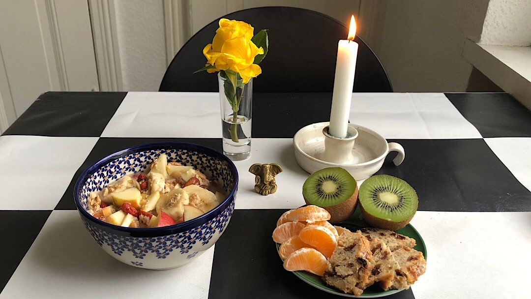 Gedeckter Tisch mit Frühstück für eine Person. Mit Kerze, Blume und kleiner Ganesha Figur.