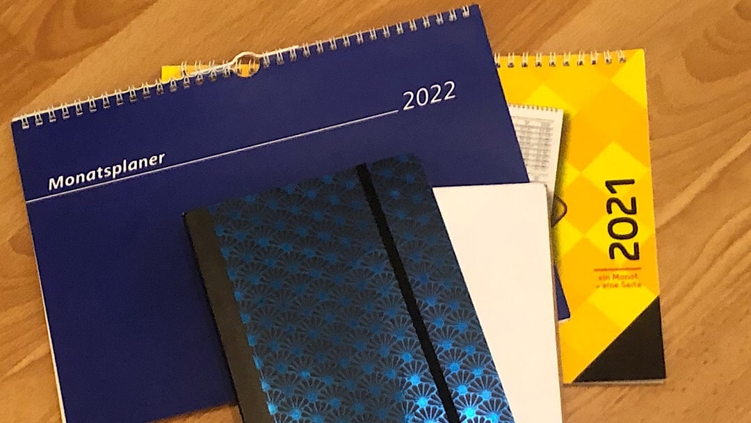 Wochenkalender von 2021 und 2022. Auf dem Holzboden liegen dazu auch noch zwei Notizbücher.